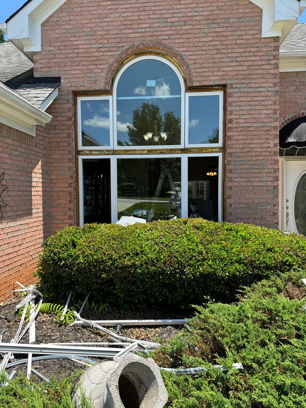 Arched window mid-install: new units set in the brick opening, old frames cleared onto the ground