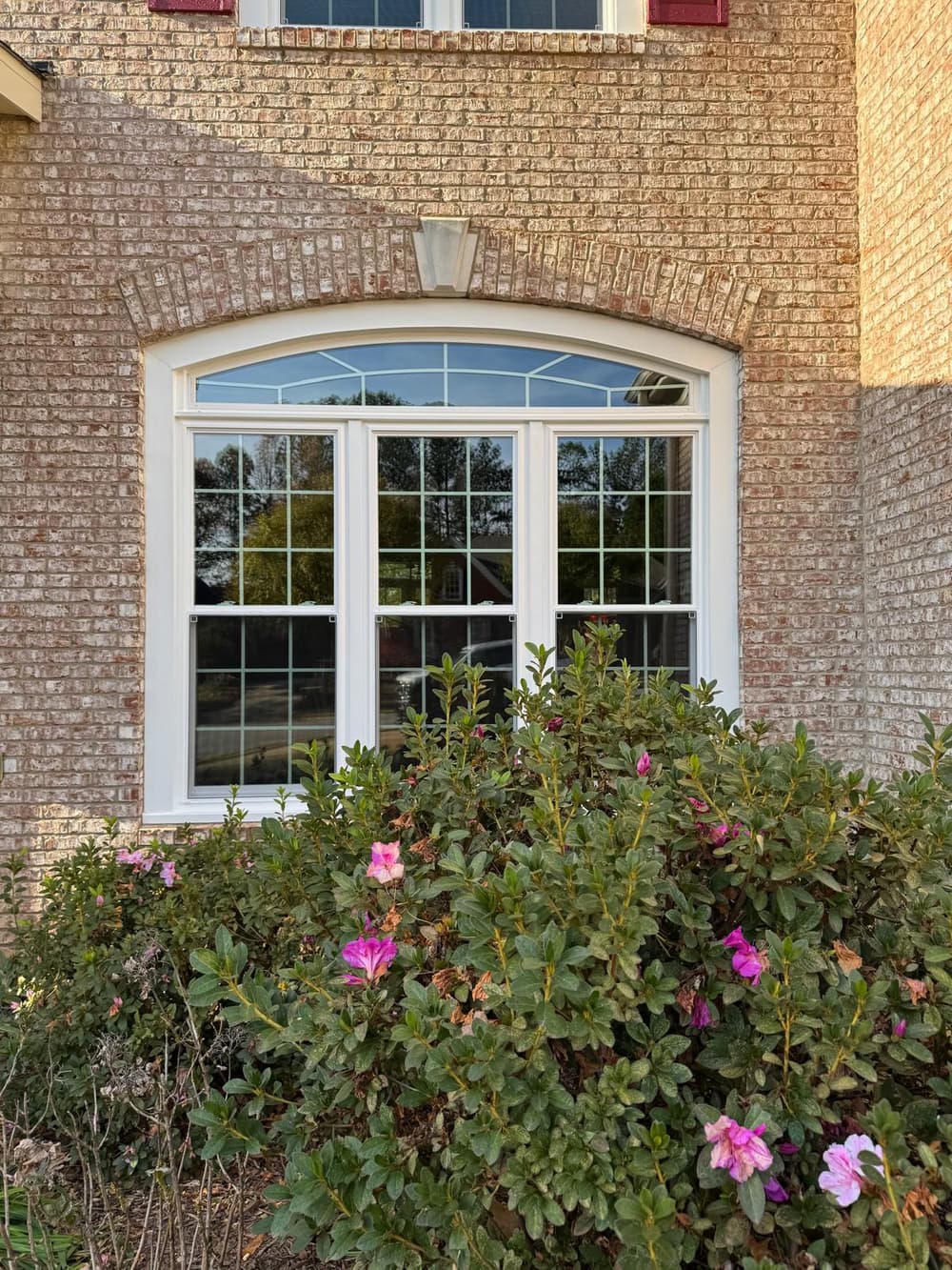 New white arched-top window with grids set in a brick wall