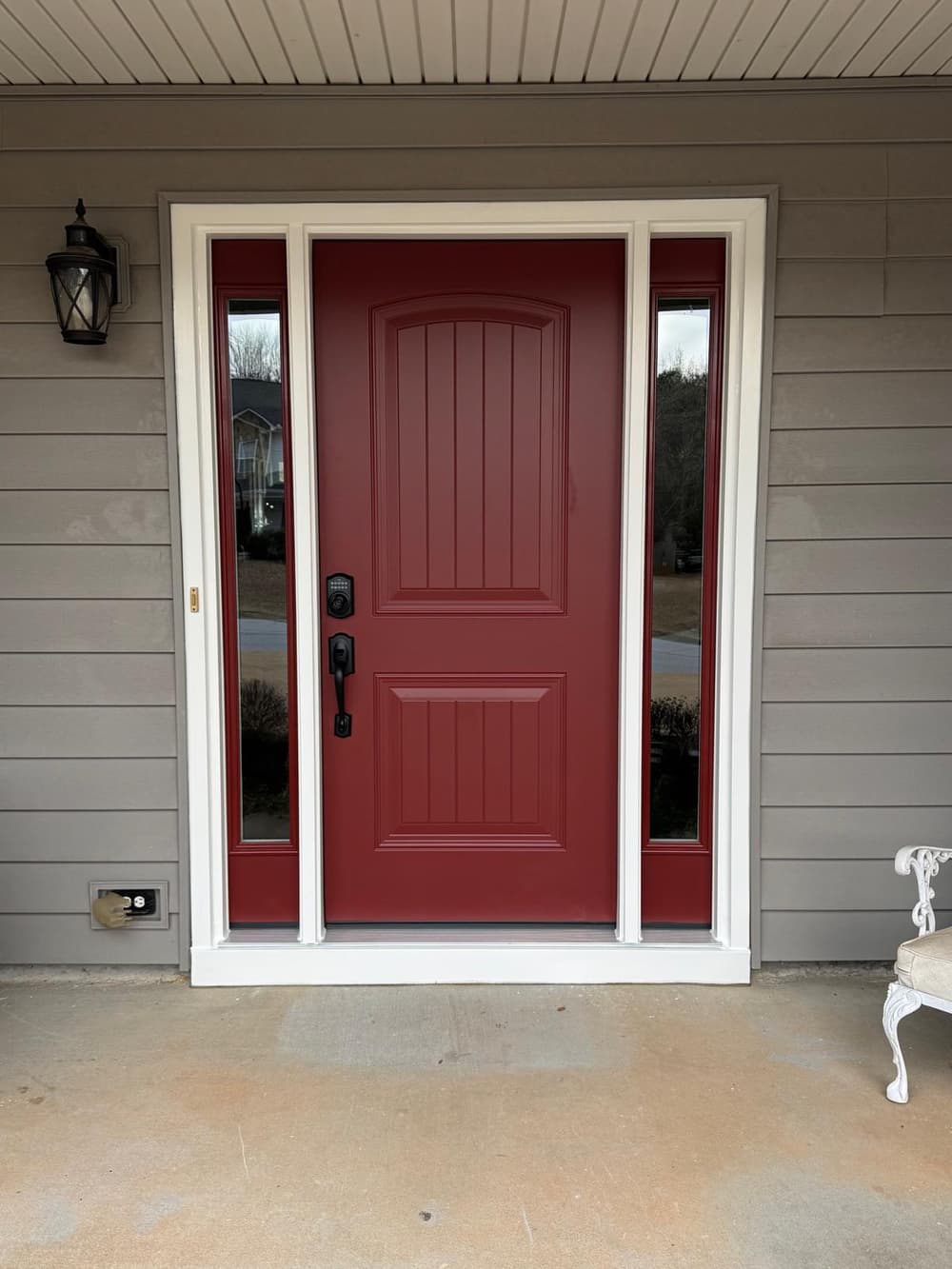 Red entry door with glass sidelites on a gray-sided porch